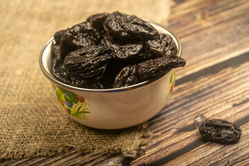 Dried prunes in a metal bowl on a wooden background. Close up.