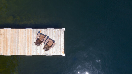 Drone aerial view of Two Adirondack chairs on a wooden dock overlooking a the calm water of a lake...