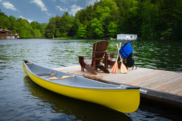 Two Adirondack chairs on a wooden dock facing the blue water of a lake in Muskoka, Ontario Canada....