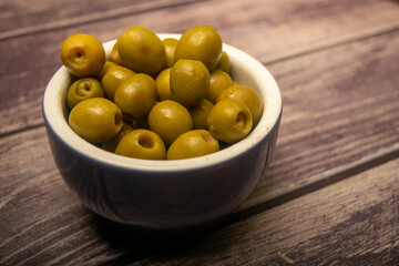 Green olives in a ceramic bowl on a wooden background . Close up.