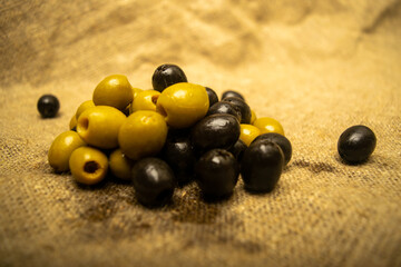 Green olives and black olives scattered on sacking with rough texture. Close up.