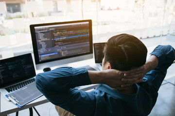 Asian programmers man are relaxing and looking at the code on the computer screen in the office.