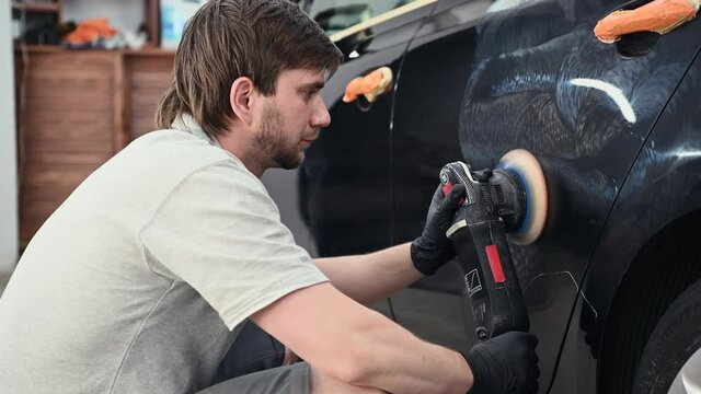 Car mechanic worker hands polishing a car side with a orbital polishing machine.