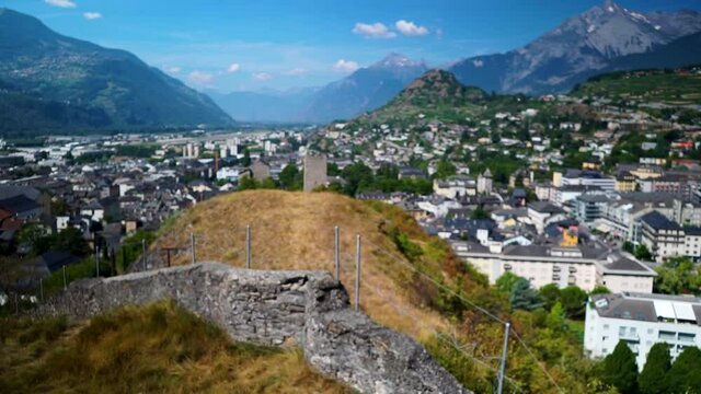 Reveal shot of Swiss Alps city in valley between beautiful mountain ranges with stone wall