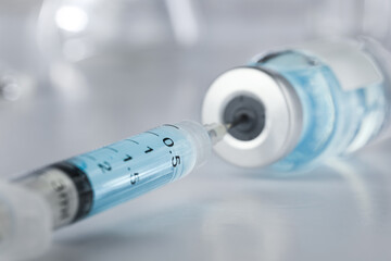 Healthcare and pharmaceutical drugs concept with syringe needle piercing the vaccine vial with blue...