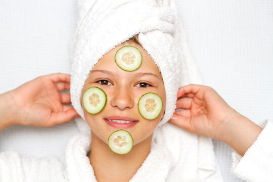 Beautiful young girl with facial mask on her face of fresh cucumber. Little girl in a towel and a bathrobe.