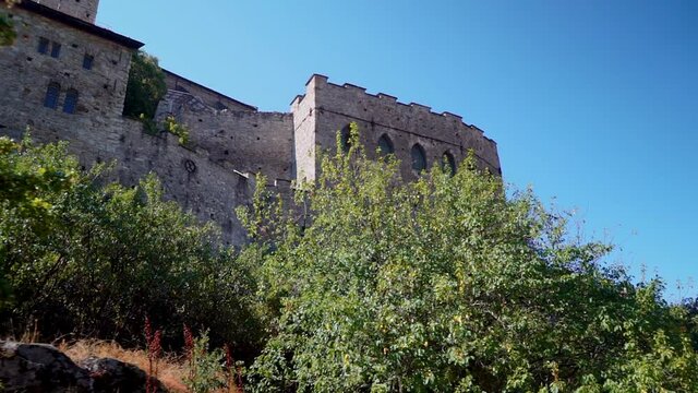 Forward dolly of old medieval castle Valere Basilica behind bushes in summer