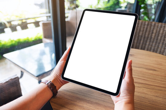 Mockup image of a woman holding black tablet pc with blank white screen on wooden table
