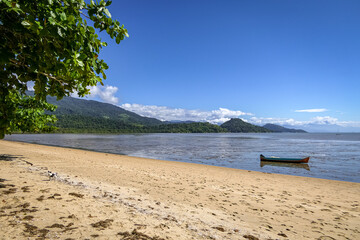 View to beach of Jabaquara with a boat on the water and mountains in background, Paraty, Brazil