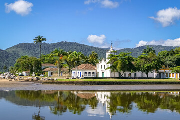 Fototapeta na wymiar Panoramic view of colonial church Igreja Nossa Senhora das Dores (Church of Our Lady of Sorrows) with water reflections and mountains in background, historic town Paraty, Brazil