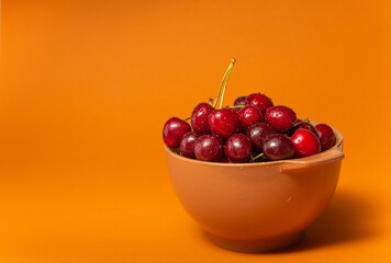 Cherries with water drops in bowl on terracota background. Fruit bowl. Delicious food. Copy space. High quality close up photo.