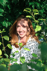 beautiful young woman happy smiling and looking through tree leaves. woman wearing trendy polka dot blouse. happy summer holidays selebration. portrait of young caucasian woman