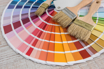 set of paint brushes roller tray and colour paper palette on wooden board