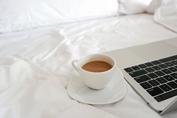 Cup of coffee beside laptop on unmade bed. Work from home concept. Copy space.