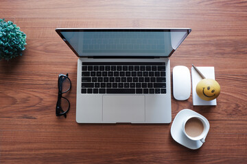Laptop, eyeglasses, cup of coffee, writing pad, pen, stress ball and computer mouse on wooden surface. Work from home concept.