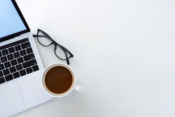 Laptop, cup of coffee and eyeglasses on white surface. Copy space.