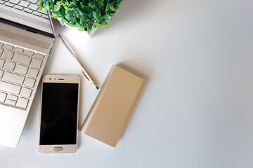 Gold laptop, smart phone, power bank and pen on white surface. Copy space.