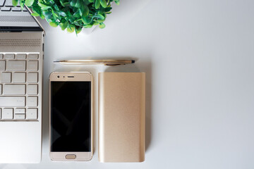 Neatly arranged gold laptop, smart phone, power bank and pen on white surface. Copy space.