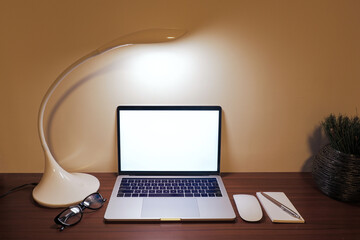 Laptop, desk lamp, eyeglasses, writing pad, pen and computer mouse on wooden desktop. Work from home concept.