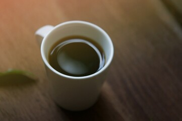 Top view of a black coffee ( americano ) in coffee cup on wood background, soft focus with sun ray light