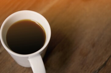 Top view of a black coffee ( americano ) in coffee cup on wood background, soft focus with sun ray light