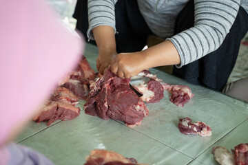 hands of adult women holding and slicing sacrificial meat during the Eid al-Adha celebration