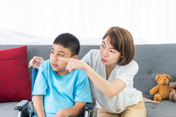 asian woman taking care disabled child on wheelchair in living room. both looking at something.