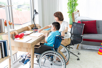 asian woman teaching disabled child on wheelchair with notebook in living room