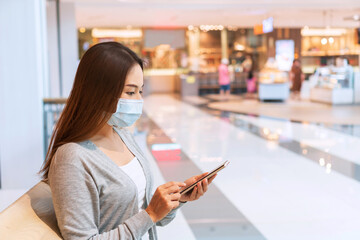 Beautiful young Asian woman wearing protective face mask in public place due to protect and reduce the spread of covid 19. New normal lifestyle, prevent pollution and disease concept