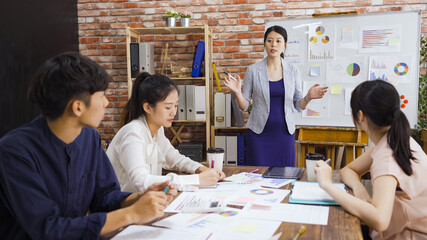 confident pregnant female manager talking with hand gesture while addressing team at board meeting. man and women colleagues sitting and making note during conference. maternity lady giving report