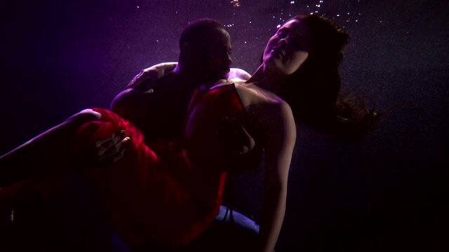 loving man and woman are floating underwater in large aquarium, guy is holding girlfriend in hands