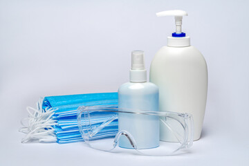 bottle of lotion, sanitizer or liquid soap, protective mask and glasses over light grey background