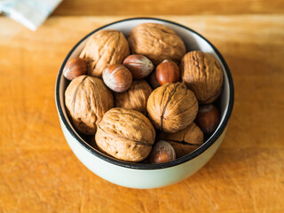 Walnuts and hazelnuts in green bowl on wooden board. Closeup