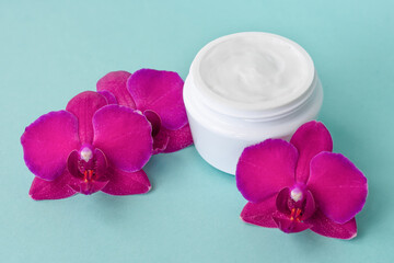 Obraz na płótnie Canvas Cream in white jar on mint background with beautiful bright magenta orchid flowers. Soft cream with orchid extract for moisturizing skin. Eco cosmetic product