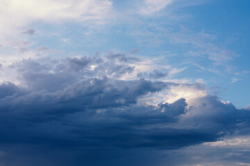 Dramatic rainy clouds on dark blue evening sky. Natural background with stormclouds and sunlights of setting sun.