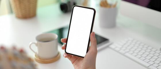 Female hand holding mock-up smartphone while standing at office desk