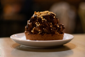 Chocolate muffin cake with nuts and choco cream on white plate on wooden table. Dessert chocolate baked treat