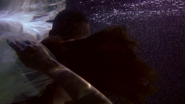 sensual man and woman are underwater in darkness, swimming and caressing, lovers in pool