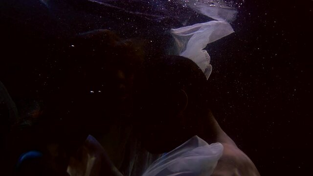 silhouette of lovers in darkness underwater, tender caress of young lovers