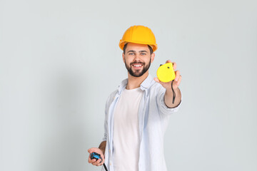 Young man with measuring tapes on light background