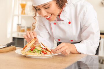 Female African-American chef with tasty dish in kitchen