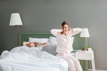 Young irritated woman in bed with snoring husband