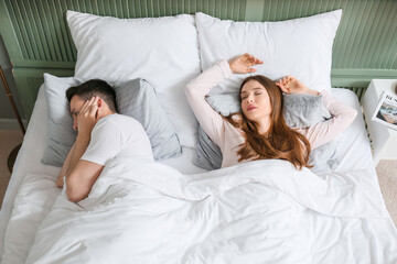 Young irritated man in bed with snoring wife