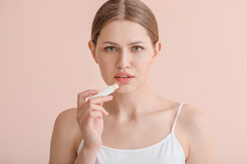 Beautiful young woman with lip balm on color background