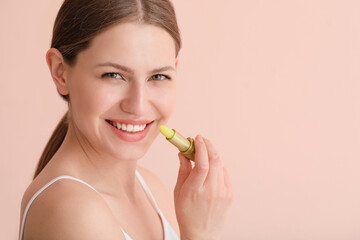 Beautiful young woman with lip balm on color background