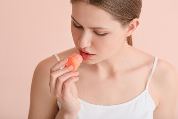Naklejka premium Beautiful young woman with lip balm on color background