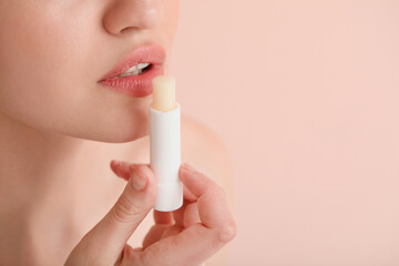 Beautiful young woman with lip balm on color background, closeup