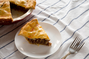 Tasty Homemade Canadian Tourtiere Meat Pie on a white plate, side view.
