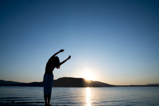 Silhouette of young Woman is stretching her body for morning sport or meditation against the beauty nature. Health and Tourism concept. 