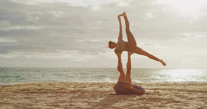 Beautiful couple practicing acro yoga at sunset on the beach, healthy lifestyle and relationship wellness